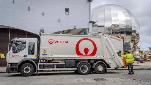 White Veolia refuse truck with red branding parked outside a building, worker in hi-vis vest at the rear