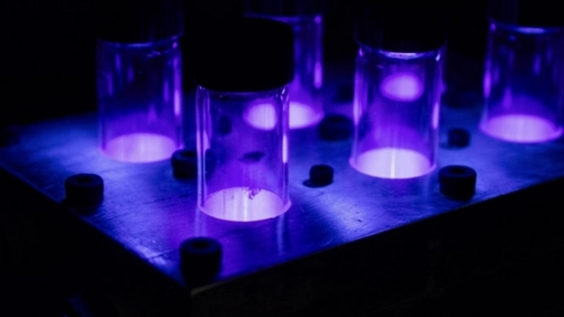 Glass laboratory vials glowing with vivid purple UV light arranged in a dark scientific testing rack